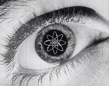 Es wird in Schwarz/Weiß die Nachaufnahme eines menschlichen Auges gezeigt. Auf der Pupille ist ein Atomstern zu sehen.