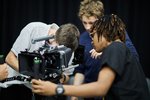 Drei Studierende sind um eine Filmkamera herum gruppiert. Sie sind in ihre Arbeit versunken.