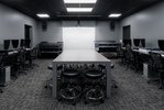 In der Mitte eines dunklen Raumes, nur mit künstlichen Licht erhellt, steht ein Tisch mit diversen Hockern darunter. An den Seiten des Raumes stehen Tische mit Computern. An der rückwärtigen Wand erkennt man große Scanner und eine weiße Leinwand.