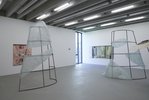 Es sind flache Arbeiten an der Wand zu sehen und in der Mitte des Raumes Skulpturen aus einem Metallgitter. Daran angebracht ist ein durchscheinendes Material.
