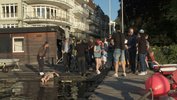 Many people stand and talk in confusion close to the water, a footbridge runs towards the viewer.