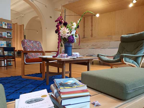 Eine gemütliche Atmosphäre wird durch unterschiedliche Sitzgelegenheiten, Regale und einen Tisch mit einem tollen Blumenbouquet erzeugt. Überall im Raum sind Bücher zu finden.