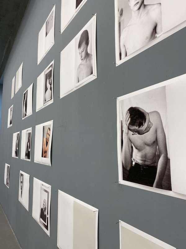 Fotografien von jungen Männern im Nahporträt hängen an einer grauen Wand.