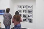 Zwei Personen stehen vor einer Wand mit 12 gerahmten Schwarz-Weiß-Fotografien.