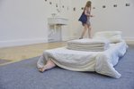 Auf dem Boden liegt eine graue Malerdecke. Darauf eine Anordnung von Bettdecken (ohne Bezug). Unter der Bettdecke schaut ein rücklingsgedrehter Fuß hervor.