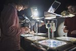Menschen stehen um Overhead-Projektoren, die eingeschaltet sind. Die Menschen malen auf Folien, die projiziert werden.