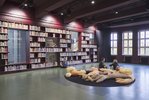 Der Bibliotheksraum wird von Studierenden als Aufenthaltsraum genutzt. Die Wände sind durch Bücherregale definiert. An der rückläufigen Wand ist ein Servicetresen zu sehen.