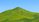 Eine Fotografie von einem grünen Hügel mit blauem Hintergrund. Ganz klein sind Menschen zu sehen, die einen kleinen Weg den Hügel hochgehen. 