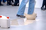 A liquid is poured onto the floor of the exhibition space, the feet and legs of the performer can be seen.