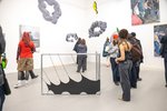 Many people stand in a room with paintings and fabric sculptures.