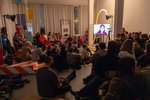 A group of visitors sits on the floor in a classroom and listens to a lecture