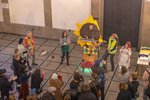 A person dressed as the sun sings along with other colorful people