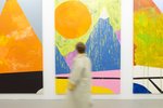 A person walks past three large-scale paintings.