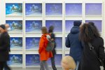 Many visitors walk past a wall with photos of the same size in the exhibition room.