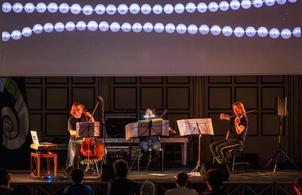 Michaela, Elen und Ruth geben ein Konzert auf der Bühne. Michaela mit Cello, die beiden anderen mit Geigen.