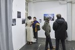Vier Personen stehen in einem Ausstellungsraum mit weißen Wänden und unterhalten sich. Die Werke an den Wänden sind meist querformatige Fotografien.