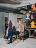 ein älterer Herr sitzt in einer Art Lagerraum locker auf einem Stuhl. Auf dem Regal hinter ihm sind mehrere Porträtbüsten in unterschiedlichen Farben, die meisten Gelb, zu sehen.