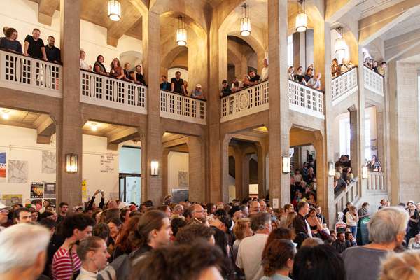 Man sieht viele Menschen in der Eingangsvorhalle und auf der Galerie, sowie auf den Treppen.