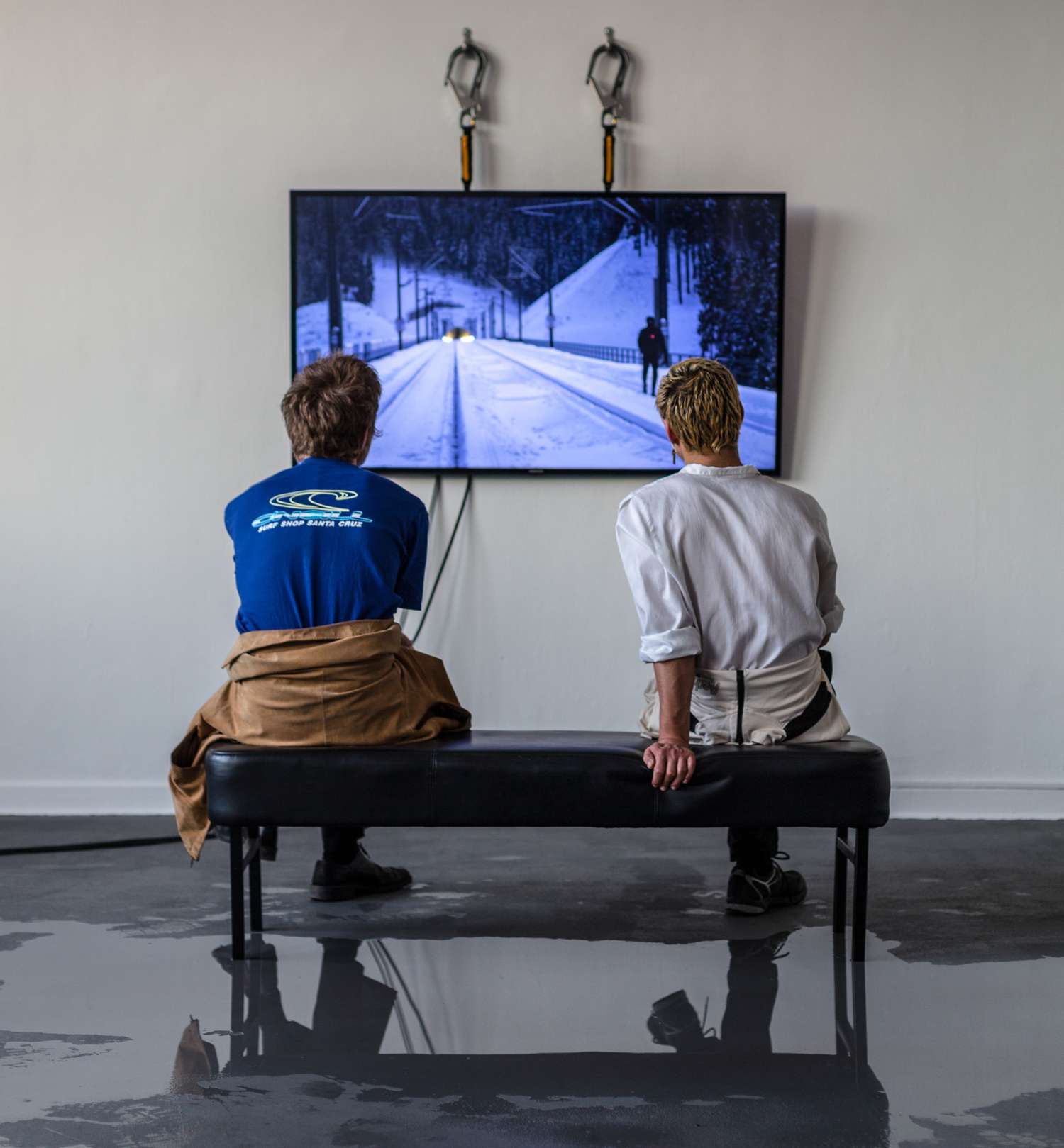 Zwei Besucher vor einem Bildschirm, Videoarbeit von Max Pilger läuft.
