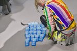 Auf grauem Boden liegt eine Ansammlung von mehreren blauen Kühlaggregaten, darüber kniet ein Besucher mit bunter Strickjacke. 