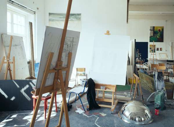 In a studio room at the HFBK, several easels, chairs as well as canvases and other objects are scattered around.