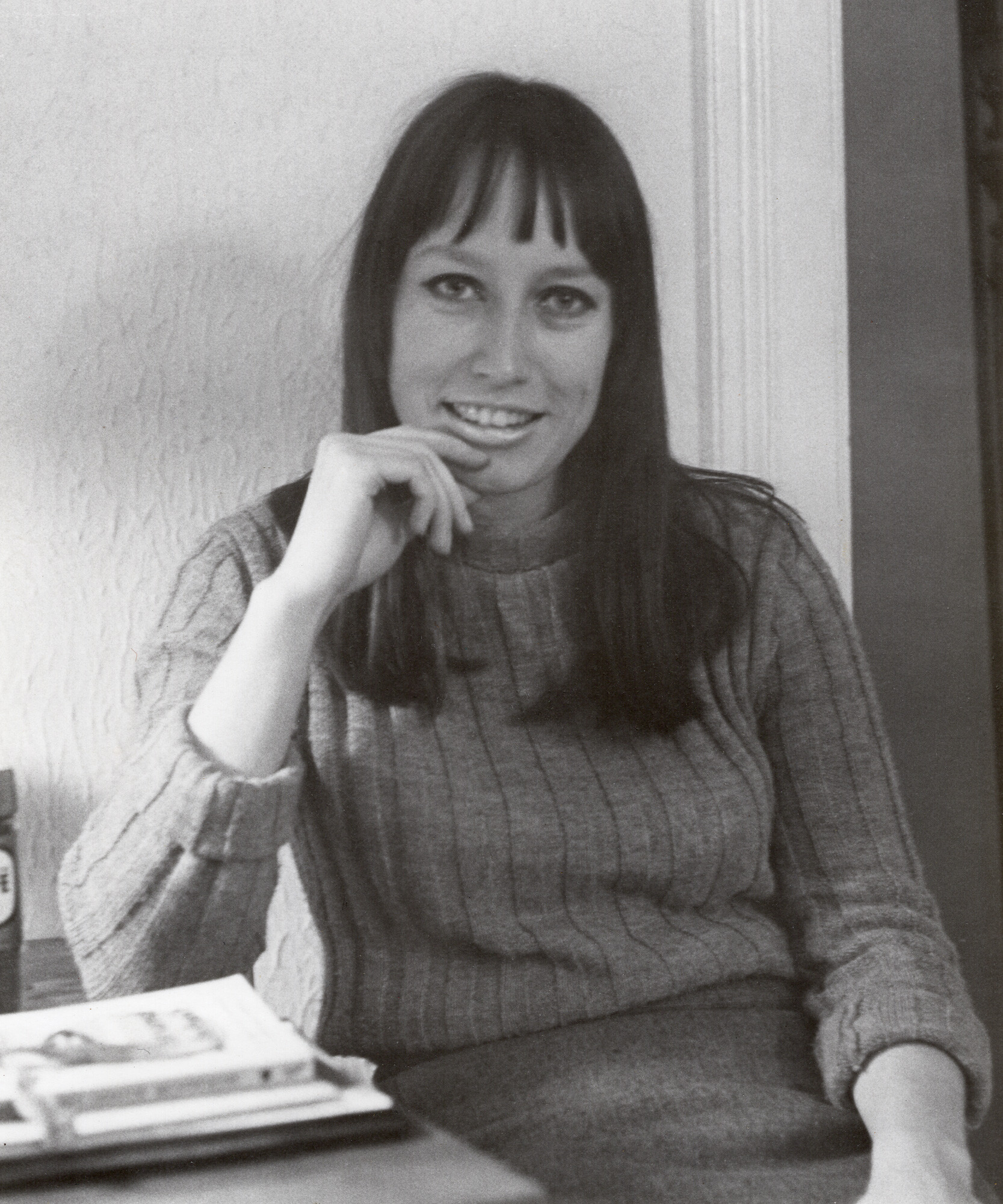 A young woman in the 1970s sits leaning against a wall.