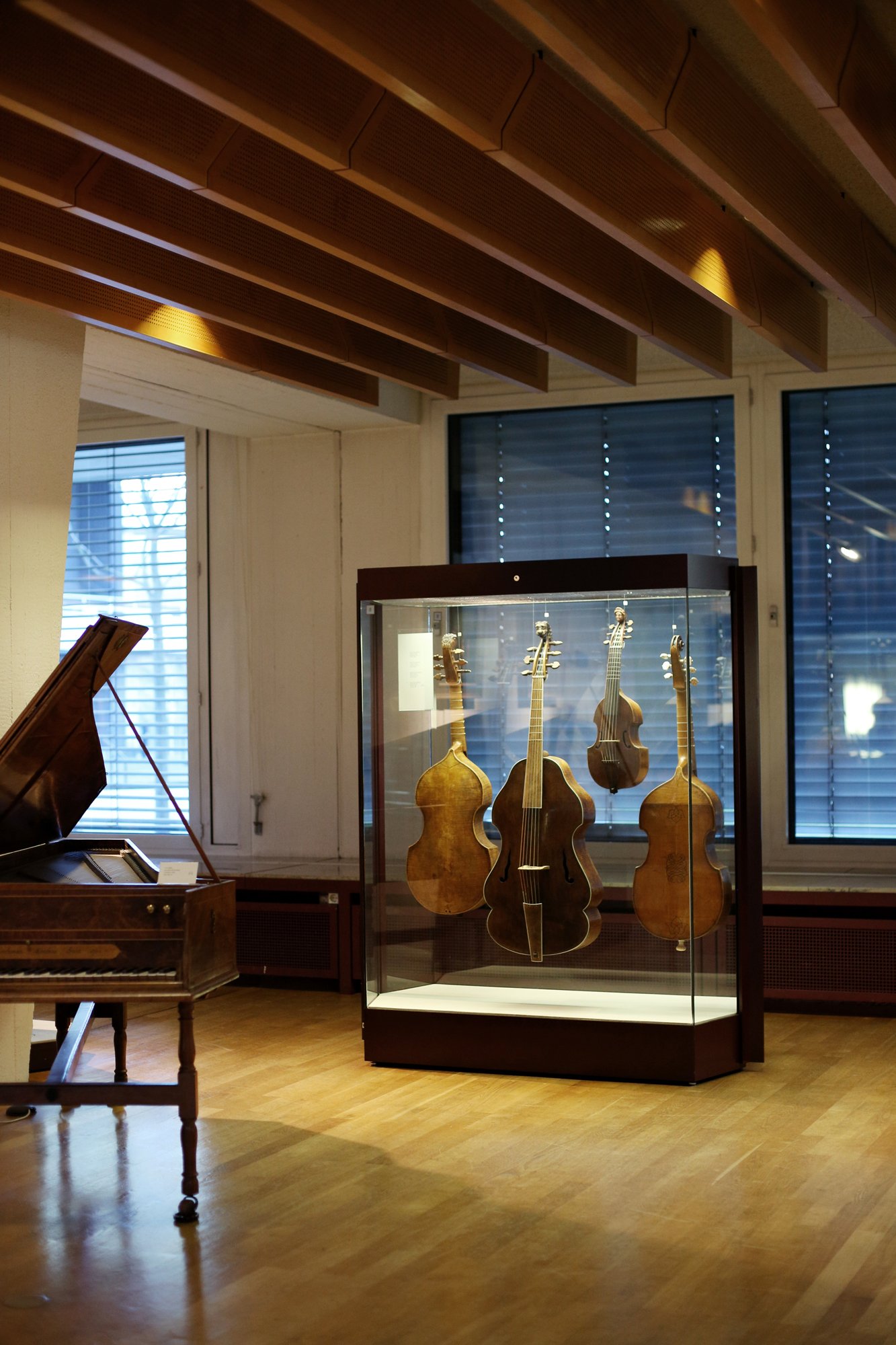 Historische Streichinstrumente in einer Glasvitrine in einem Museum, daneben ein altes Tasteninstrument in einem Ausstellungsraum mit Holzdecke.