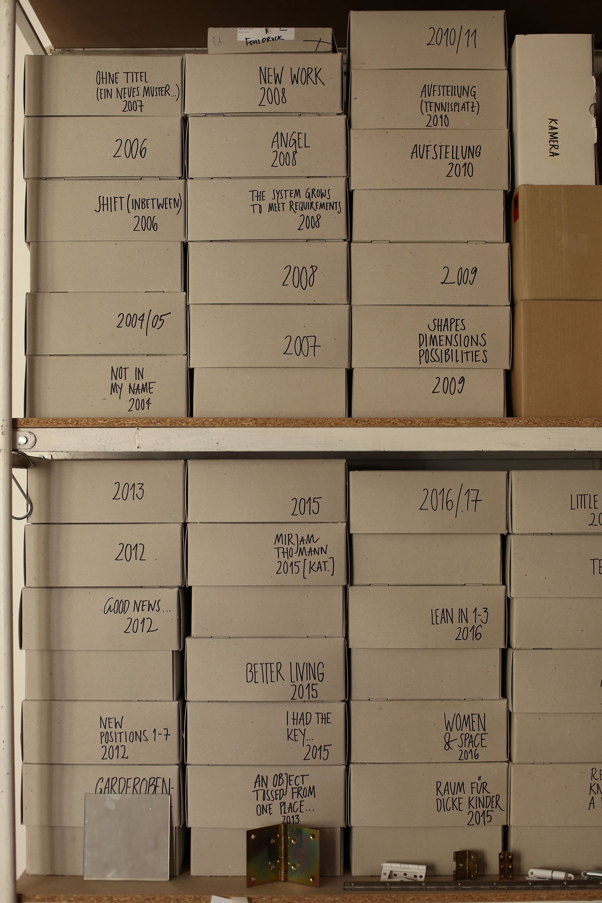 Shelf filled with tightly stacked grey archive boxes, handwritten with project titles and year labels.