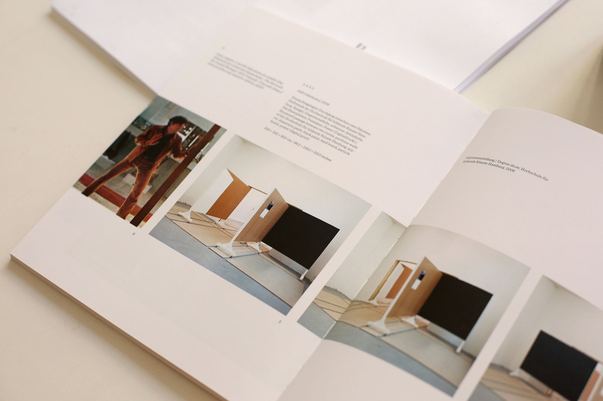 Open exhibition catalog containing text and four photographs of an installation featuring wooden panels and black board surfaces in a gallery space.
