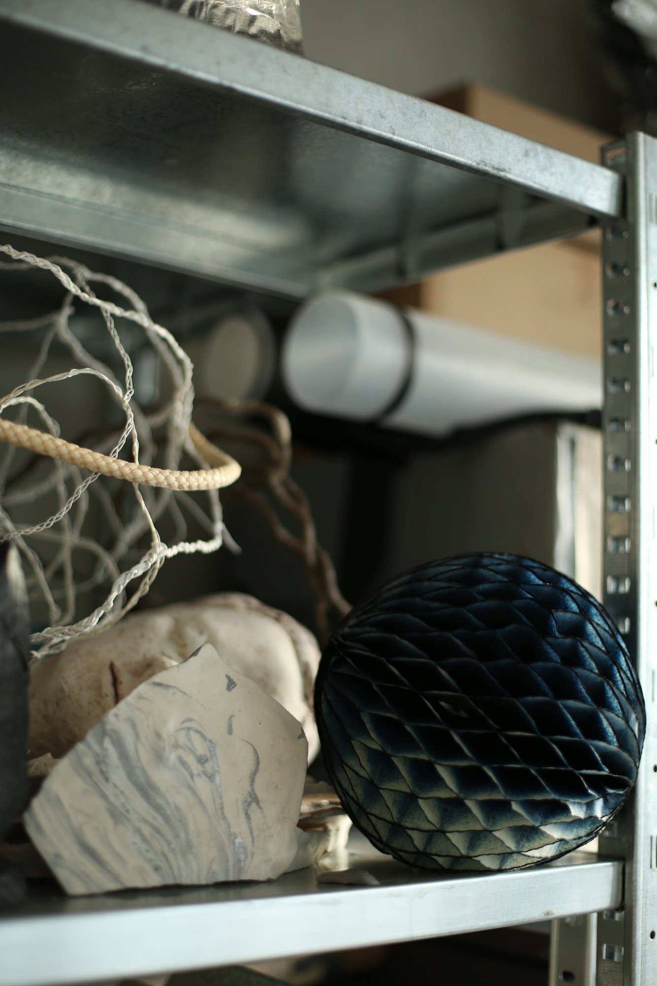 Metallregal mit verschiedenen Materialien, darunter ein dunkles wabenförmiges Objekt, helle Steine und drahtartige Strukturen.