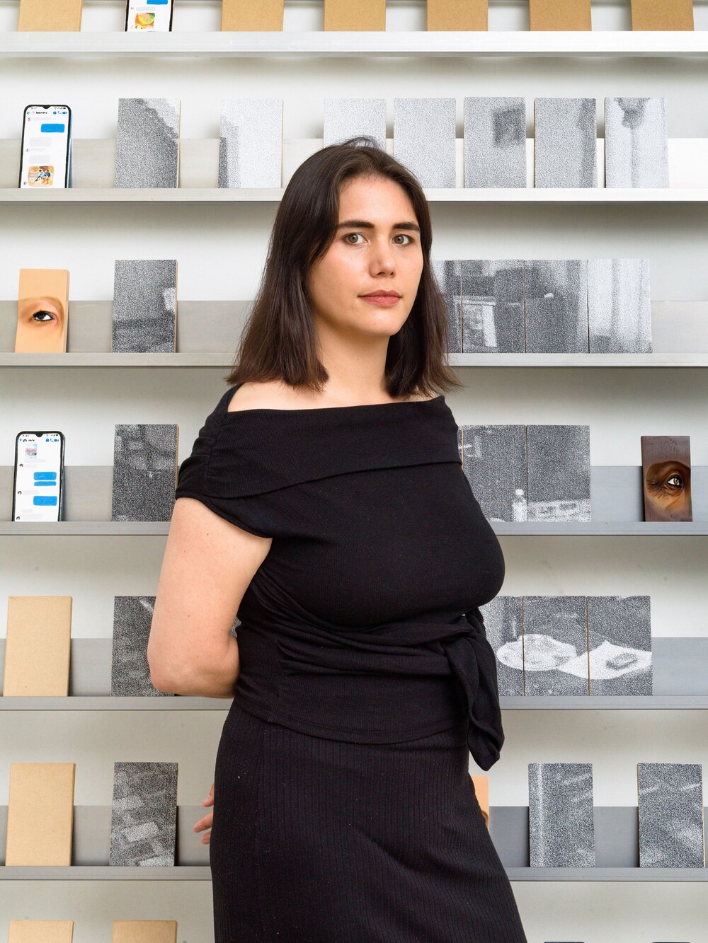 Portrait of a woman with shoulder-length dark hair standing in front of shelves displaying small image objects.