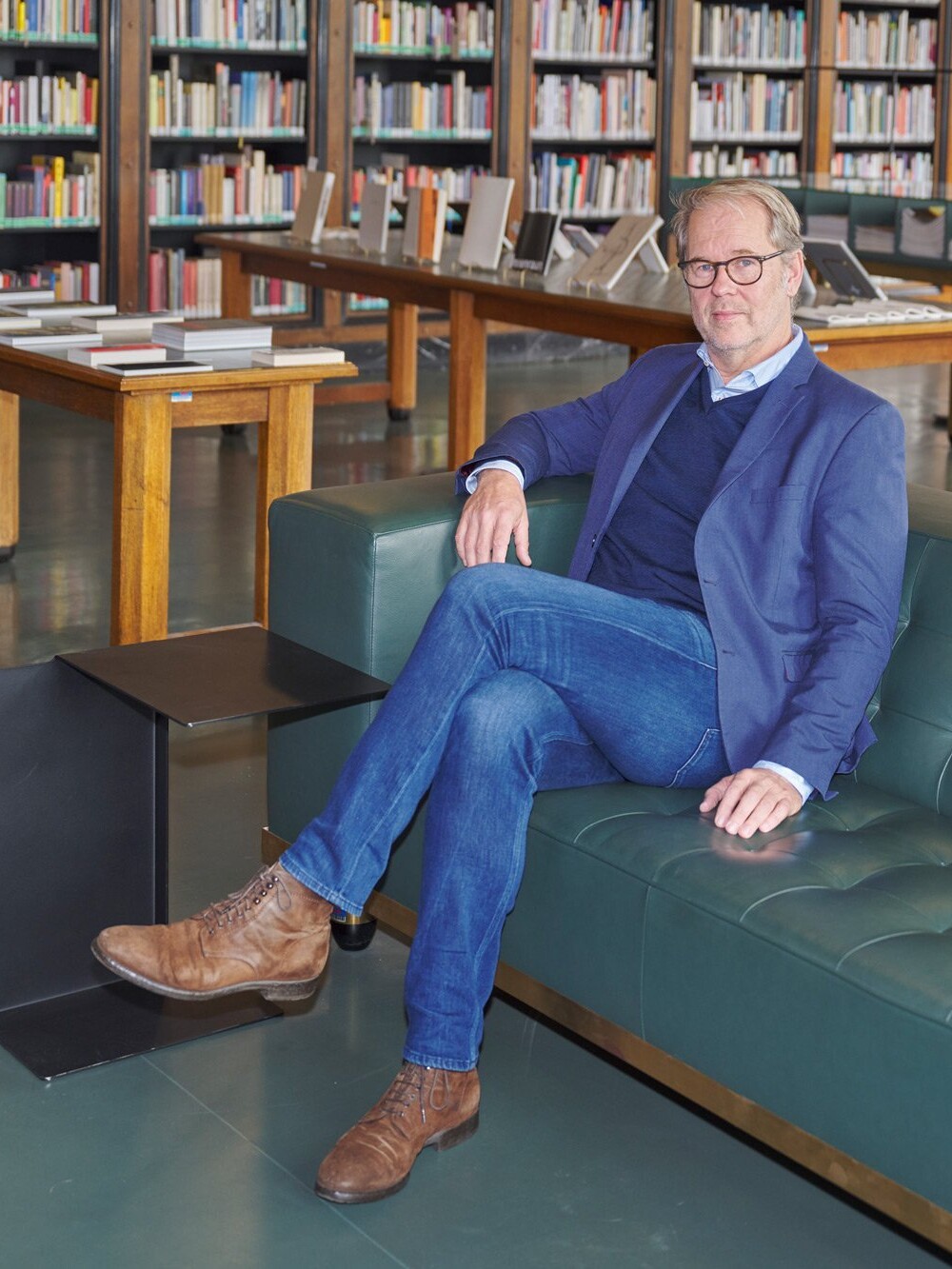 Man sitting on a sofa in a library, surrounded by bookshelves and display tables.