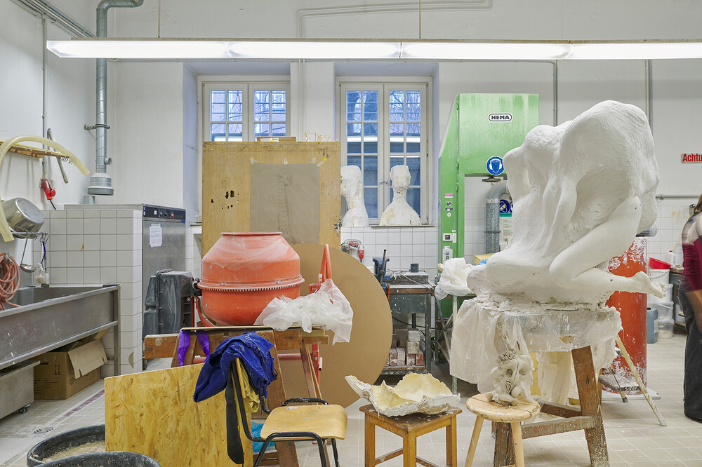 A large unfinished plaster figure on a stand, worktables with molds and supplies, and studio equipment arranged throughout the room.