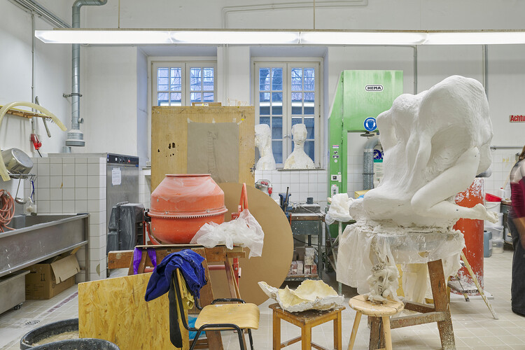 A large unfinished plaster figure on a stand, worktables with molds and supplies, and studio equipment arranged throughout the room.