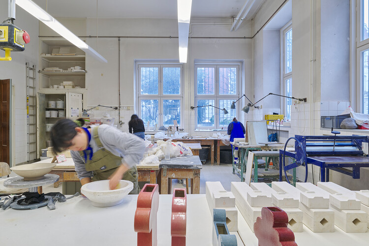 A person is working on a ceramic bowl; in the background, two other people are working as well.