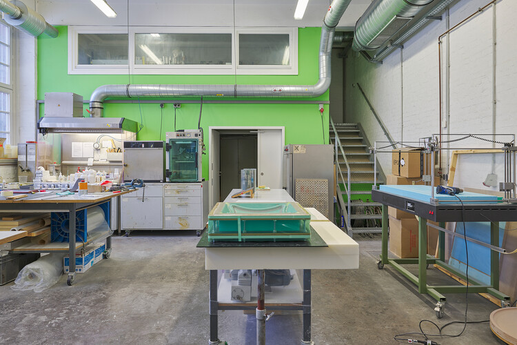 View into the workshop with a green wall; in front of it are tables and workbenches with materials laid out on them.