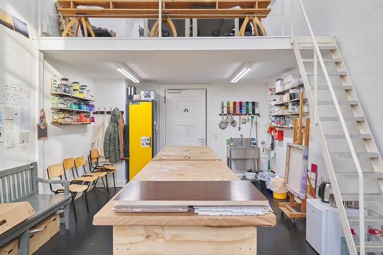 A room with a staircase, a large table, and paint cans.