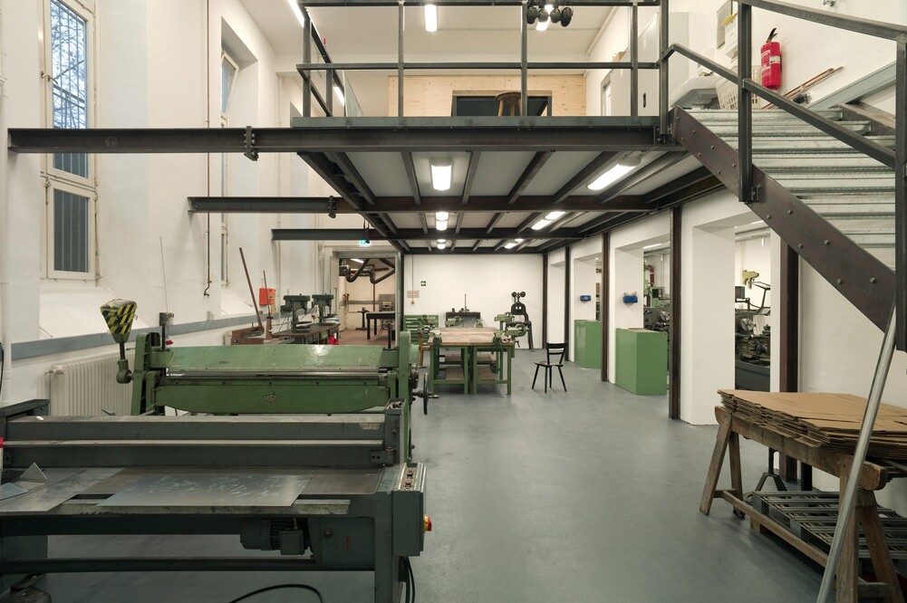 Metal cutting machines in a room with a staircase leading up to a mezzanine and workbenches.