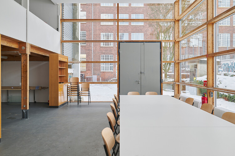 A glass pavilion with large windows, a white table in the center, and a clearly visible gallery level at the side.