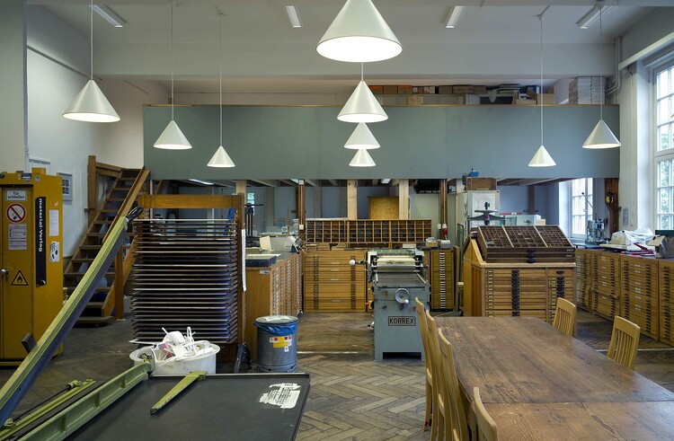 Cutting machine, type cases with letterpress type, and a worktable with chairs.