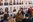 Many people stand in front of a wall with portrait photographs